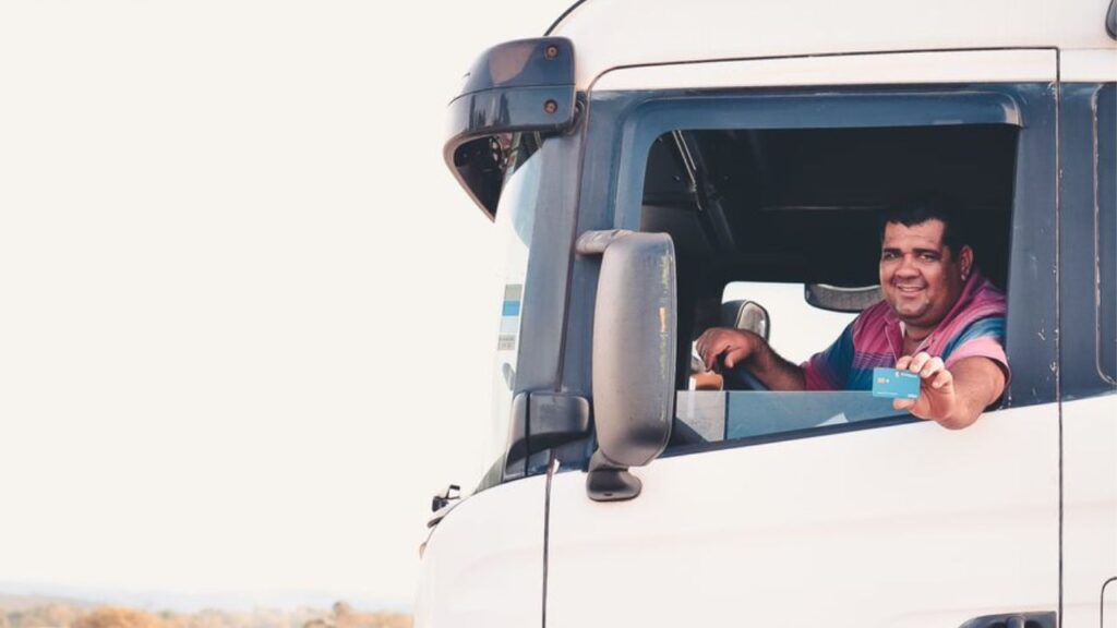 Caminhoneiros dentro do caminhão, sorrindo e mostrando um cartão da conta digital Frotabank