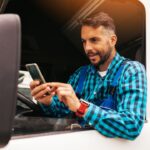 Conta digital MEI: caminhoneiro n ajanela do caminhão, mexendo em um celular